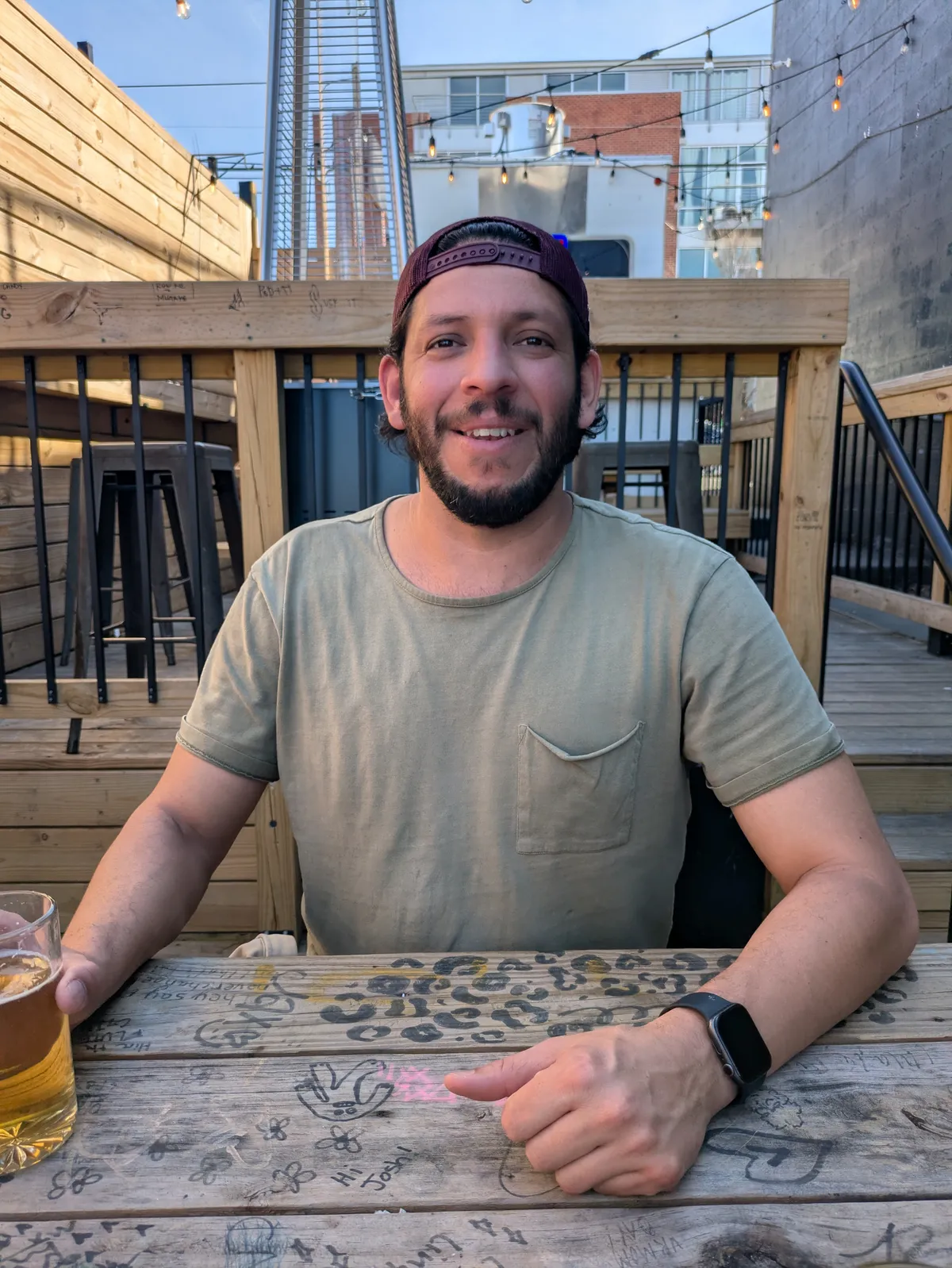 Juan Martinez grinning over a beer at a graffiti-covered patio table at Ernie's