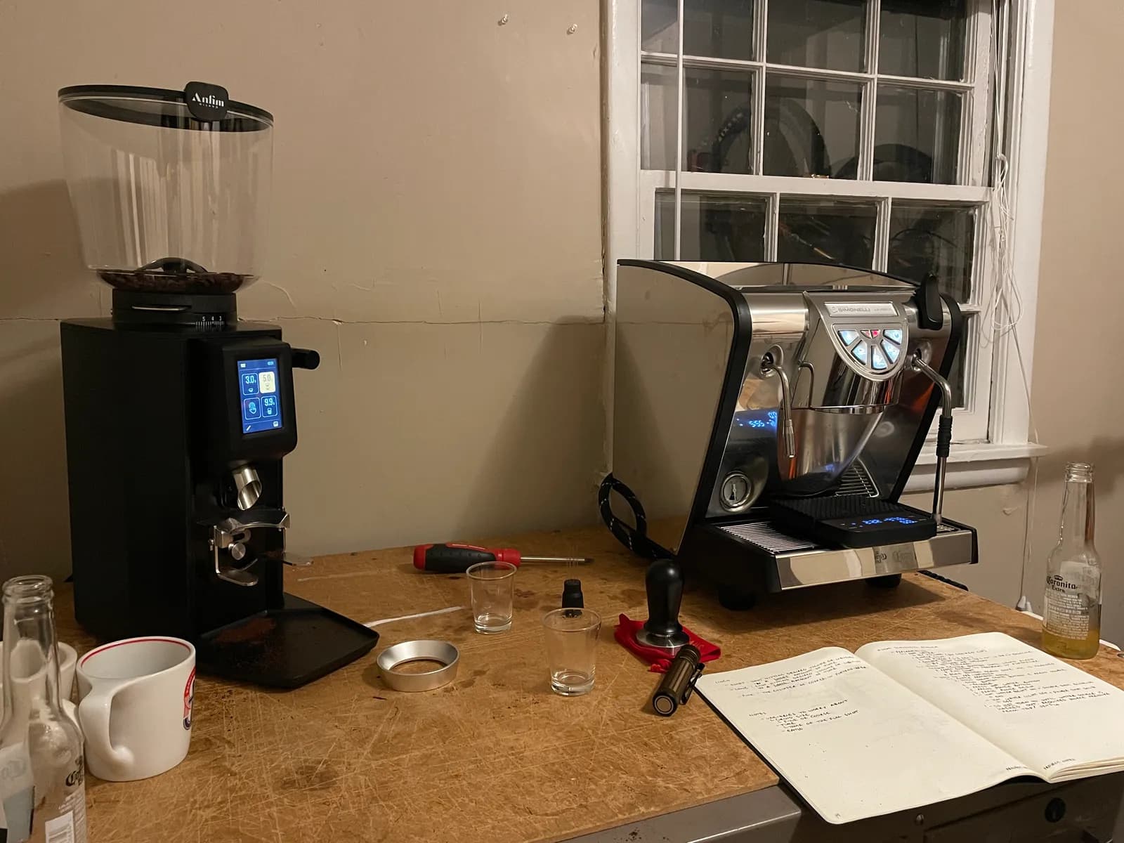 Late-night first programming of the grinder and espresso machine, with a notebook of dial-in notes open on the bench