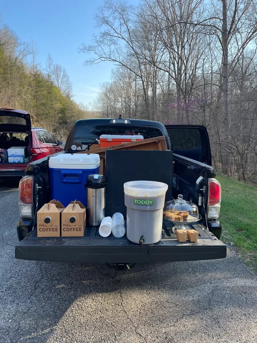 Truck bed loaded with the El Gato Negro rig at R.A.D. 100 — cold brew bucket, coolers, coffee boxes, and a cake dome on the tailgate