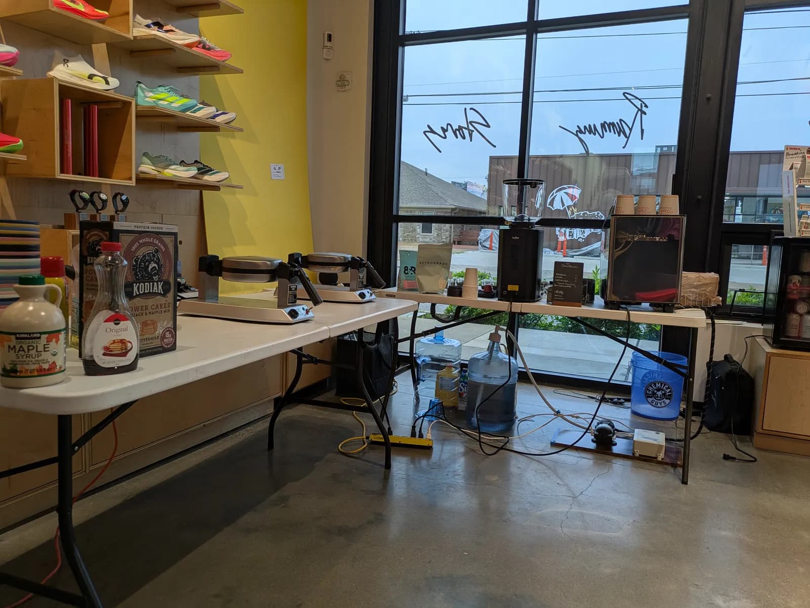 The first El Gato Negro setup on day one — espresso machine, grinder, and water jugs rigged under folding tables at The Exchange running store